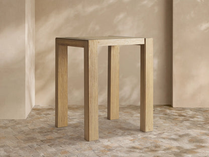 Light brown, rectangular Canyon Outdoor Teak Bar Table with natural wood grain and sturdy square legs, standing against a neutral wall.
