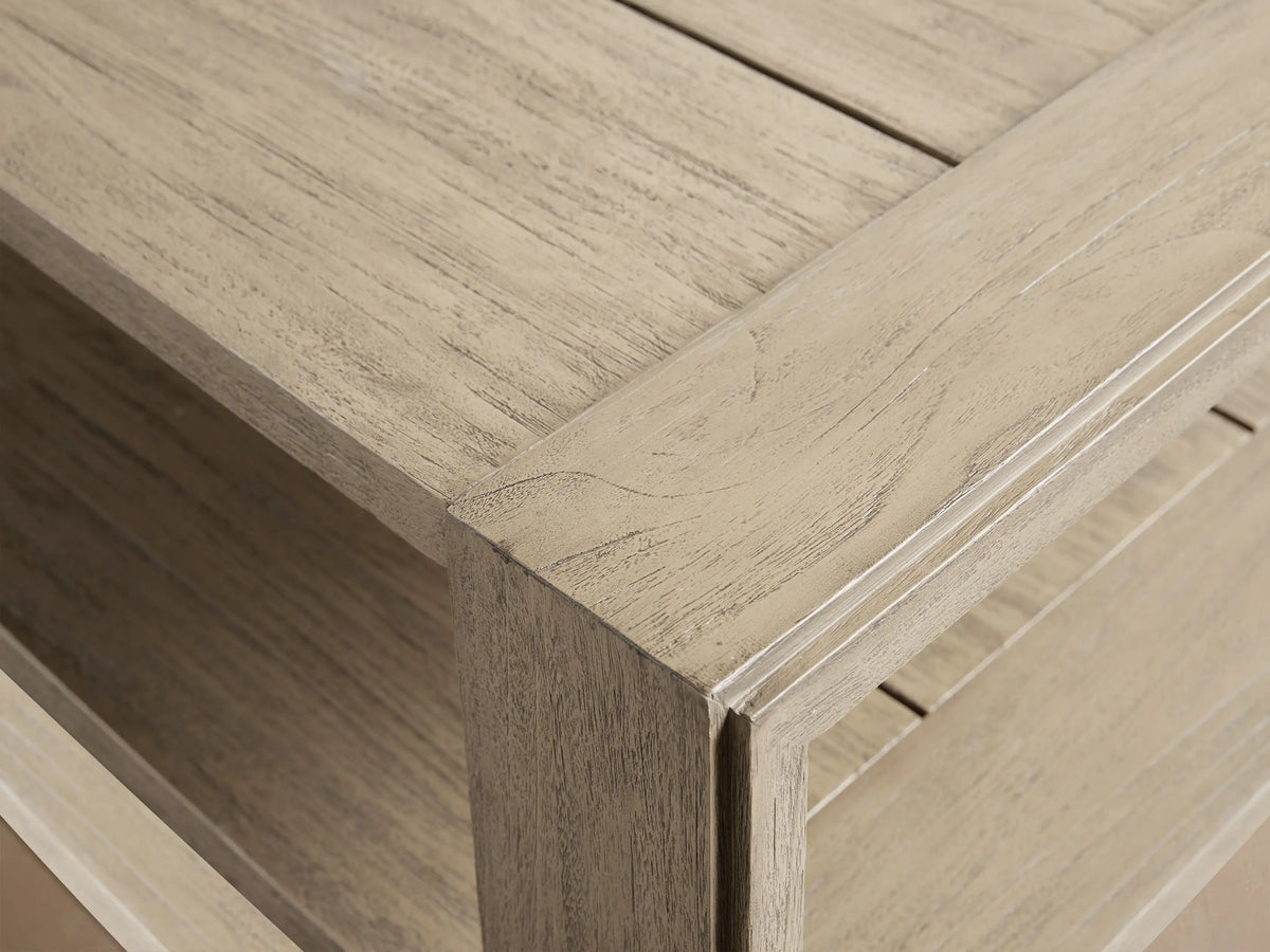 Canyon Outdoor Teak Coffee Table. Rectangular, two-tiered light greyish-brown distressed teak table on a patterned patio surface.
