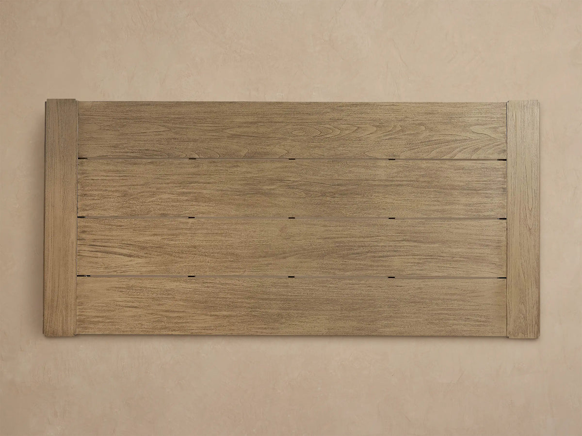 Close-up of a weathered light brown Canyon Outdoor Teak Dining Table corner, showing plank details and wood grain.