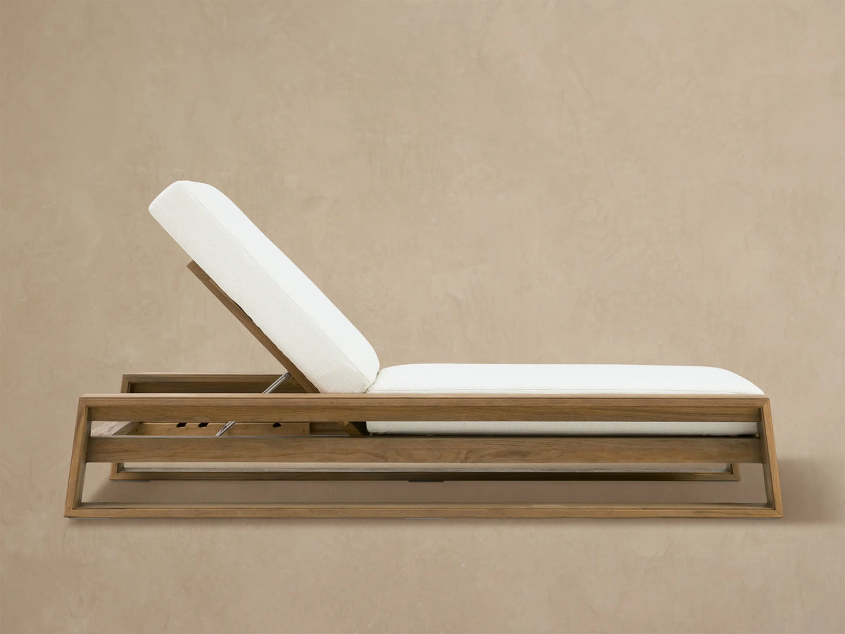 Canyon Weathered Fawn Outdoor Teak Chaise with white Eden Snow cushions, back elevated, on a light stone patio.