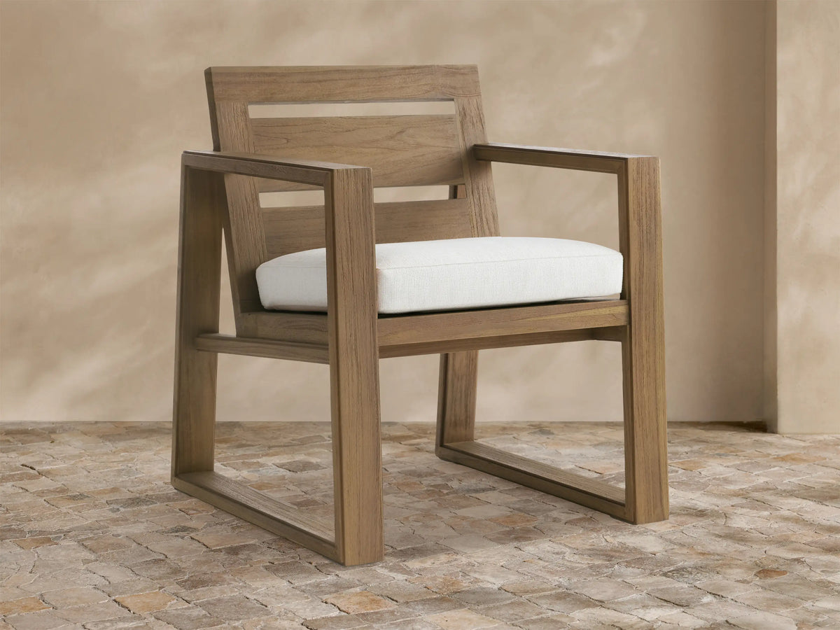 Canyon Outdoor Teak Dining Arm Chair in Eden Snow: Modern light brown teak chair with a white cushion, angled on a stone floor.