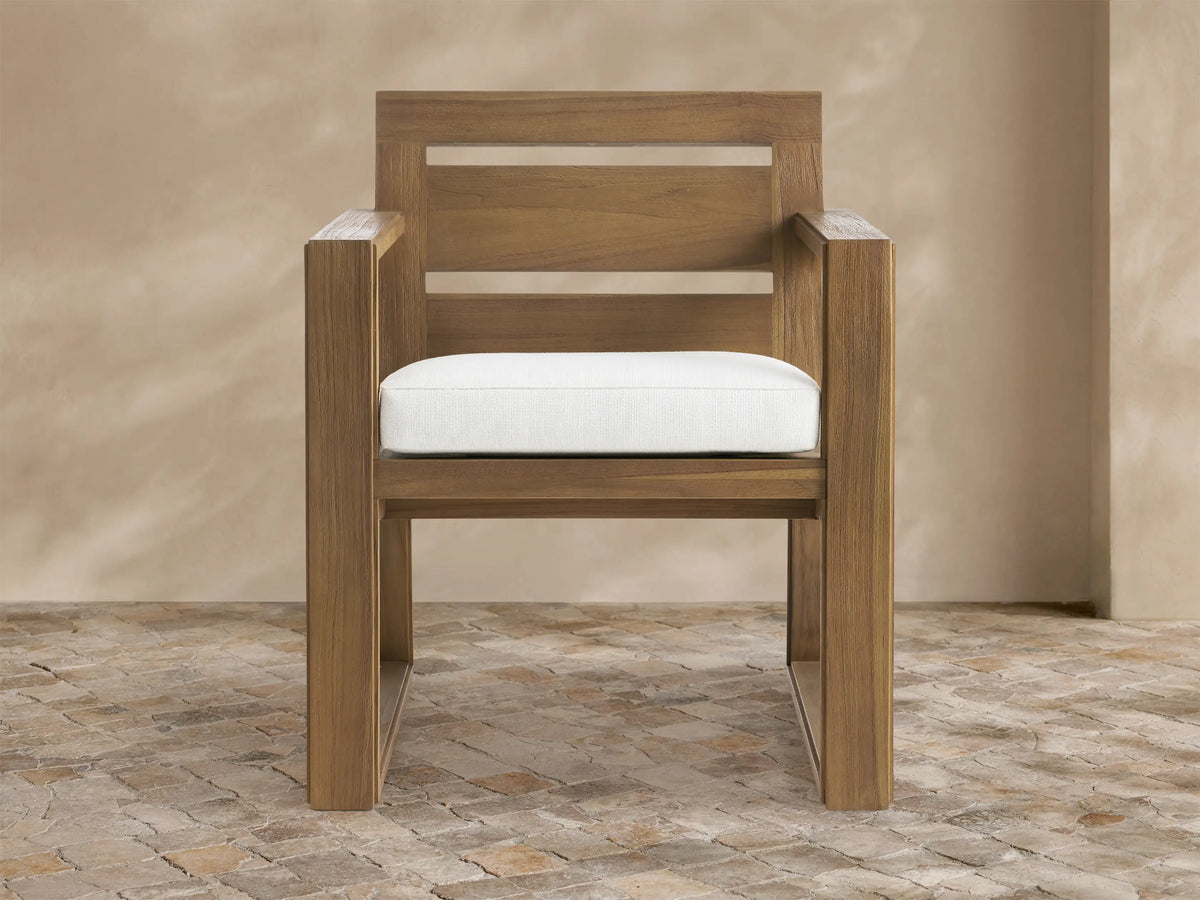 Canyon Outdoor Teak Dining Arm Chair in Eden Snow: Modern light brown teak chair with a white cushion, angled on a stone floor.