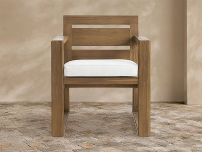 Canyon Outdoor Teak Dining Arm Chair in Eden Snow: Modern light brown teak chair with a white cushion, angled on a stone floor.