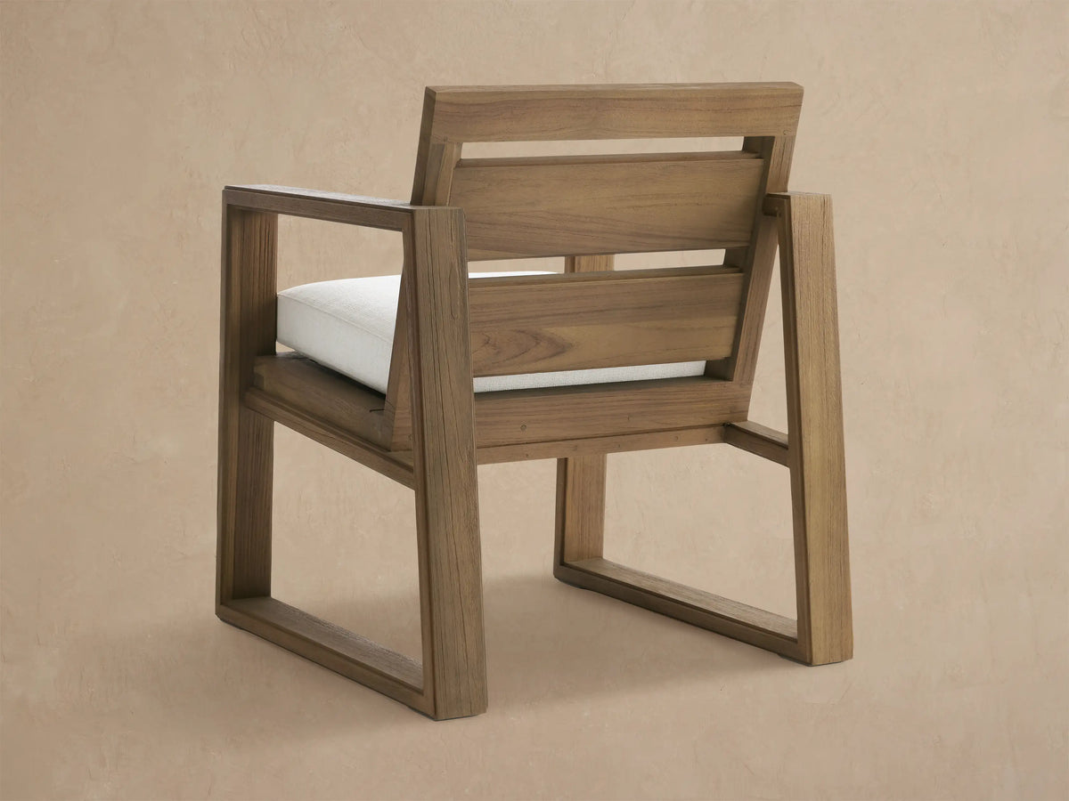 Close-up of a Canyon Outdoor Teak Dining Arm Chair in Eden Snow, with a brown teak wood frame and a textured white seat cushion.
