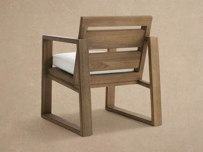 Close-up of a Canyon Outdoor Teak Dining Arm Chair in Eden Snow, with a brown teak wood frame and a textured white seat cushion.