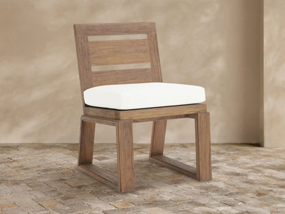 Canyon Outdoor Teak Dining Side Chair: natural teak wood, slatted back, white Eden Snow cushion, sitting on a stone floor.