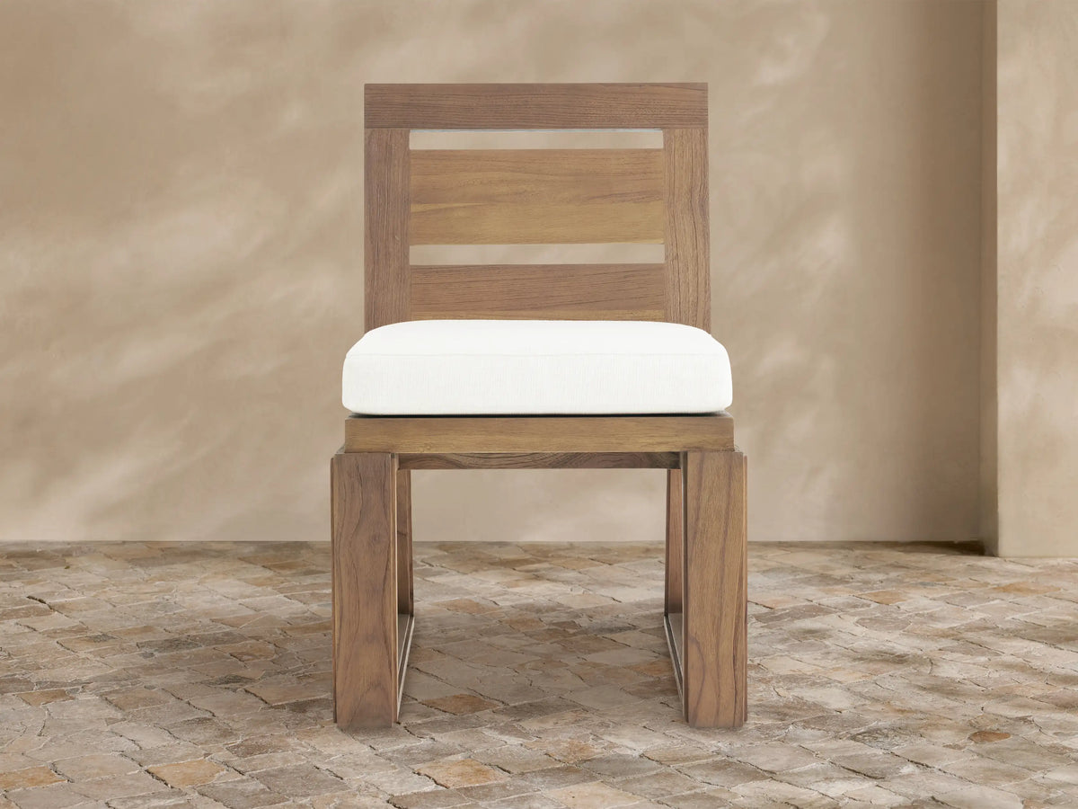 Canyon Outdoor Teak Dining Side Chair: natural teak wood, slatted back, white Eden Snow cushion, sitting on a stone floor.