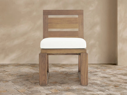 Canyon Outdoor Teak Dining Side Chair: natural teak wood, slatted back, white Eden Snow cushion, sitting on a stone floor.