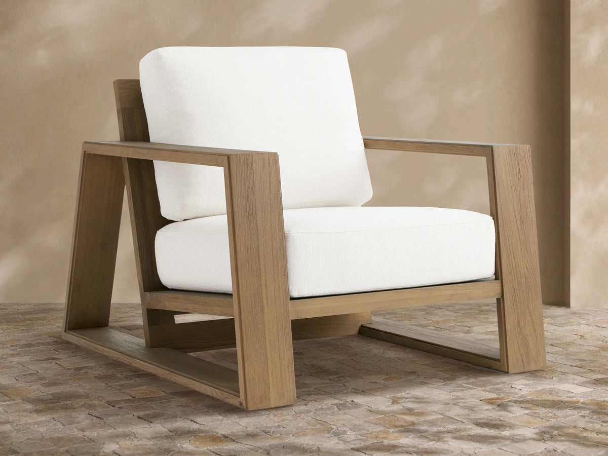 Canyon Outdoor Teak Lounge Chair, light brown teak wood frame, thick white cushions, angled on a beige tiled patio.