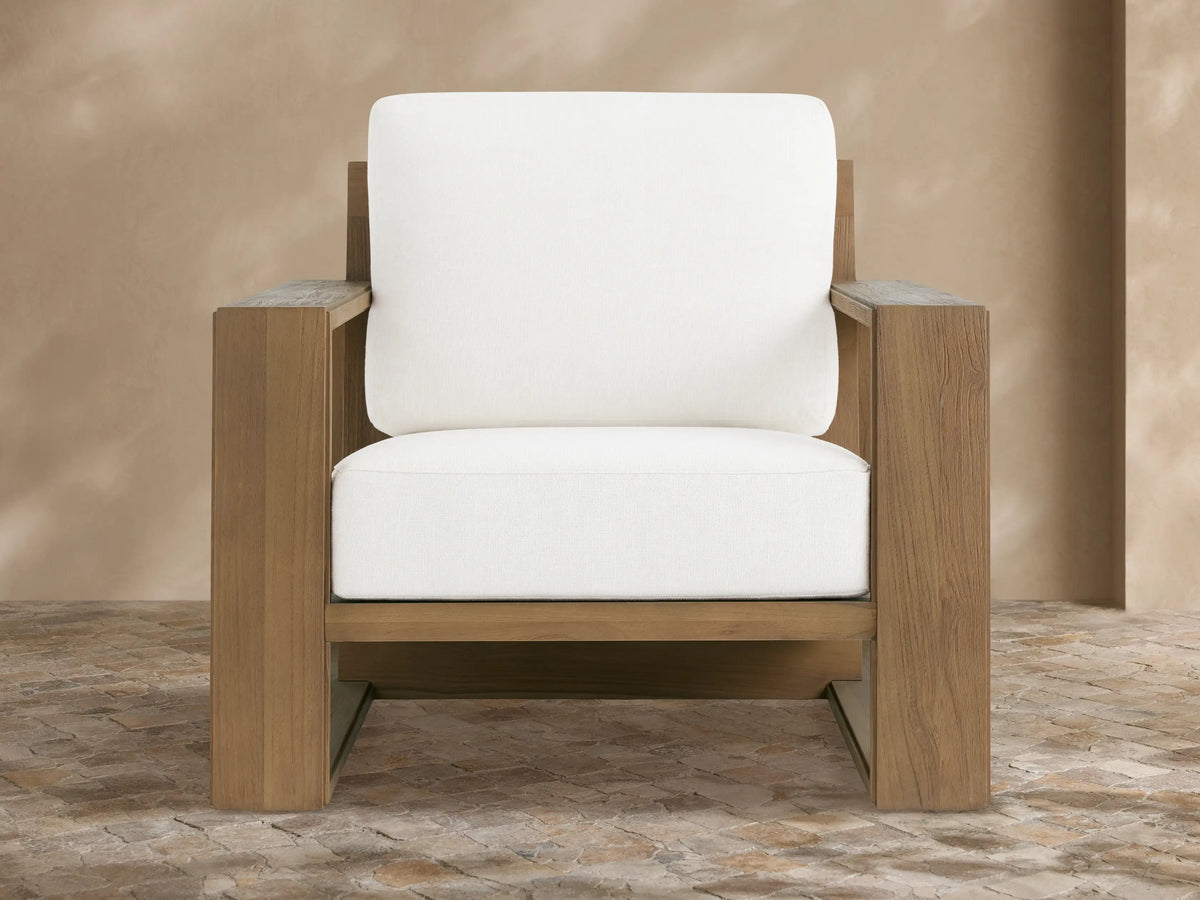 Canyon Outdoor Teak Lounge Chair, light brown teak wood frame, thick white cushions, angled on a beige tiled patio.