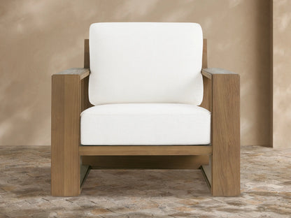 Canyon Outdoor Teak Lounge Chair, light brown teak wood frame, thick white cushions, angled on a beige tiled patio.