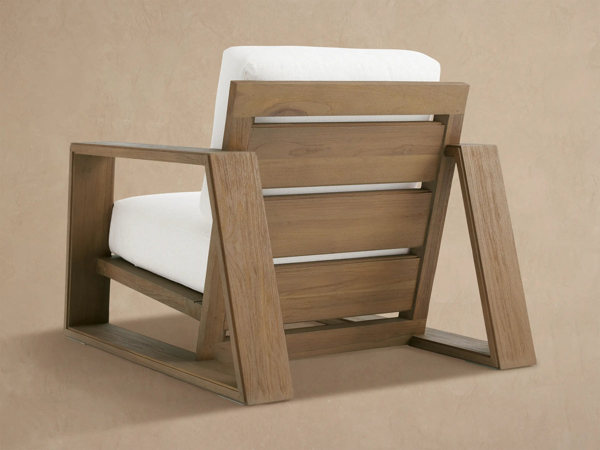 Close-up of Canyon Outdoor Teak Lounge Chair: rustic brown wood armrest with visible grain, contrasting with plush white cushions.
