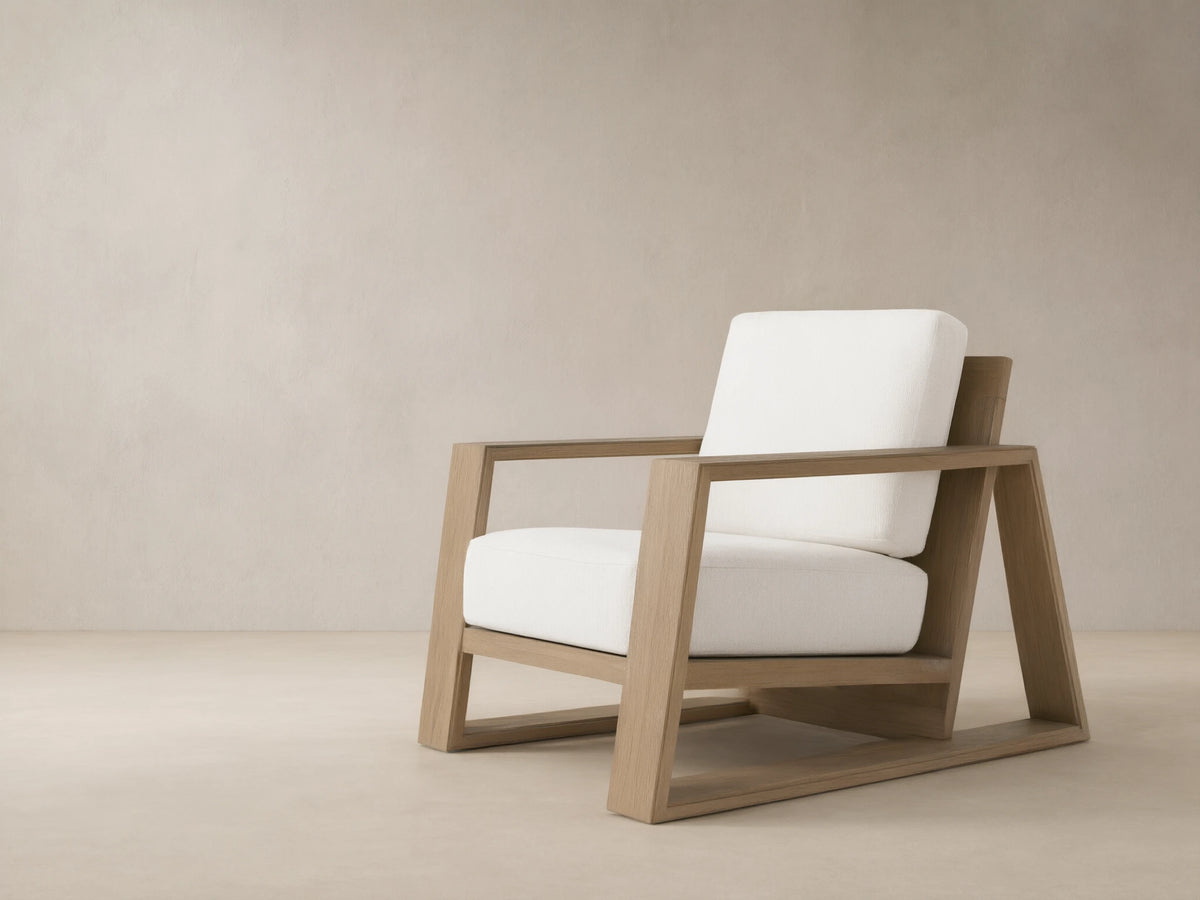 Canyon Outdoor Teak Lounge Chair, light brown teak wood frame, thick white cushions, angled on a beige tiled patio.
