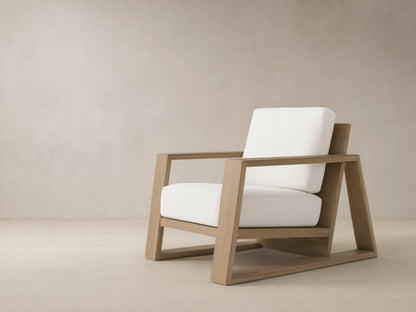Canyon Outdoor Teak Lounge Chair, light brown teak wood frame, thick white cushions, angled on a beige tiled patio.