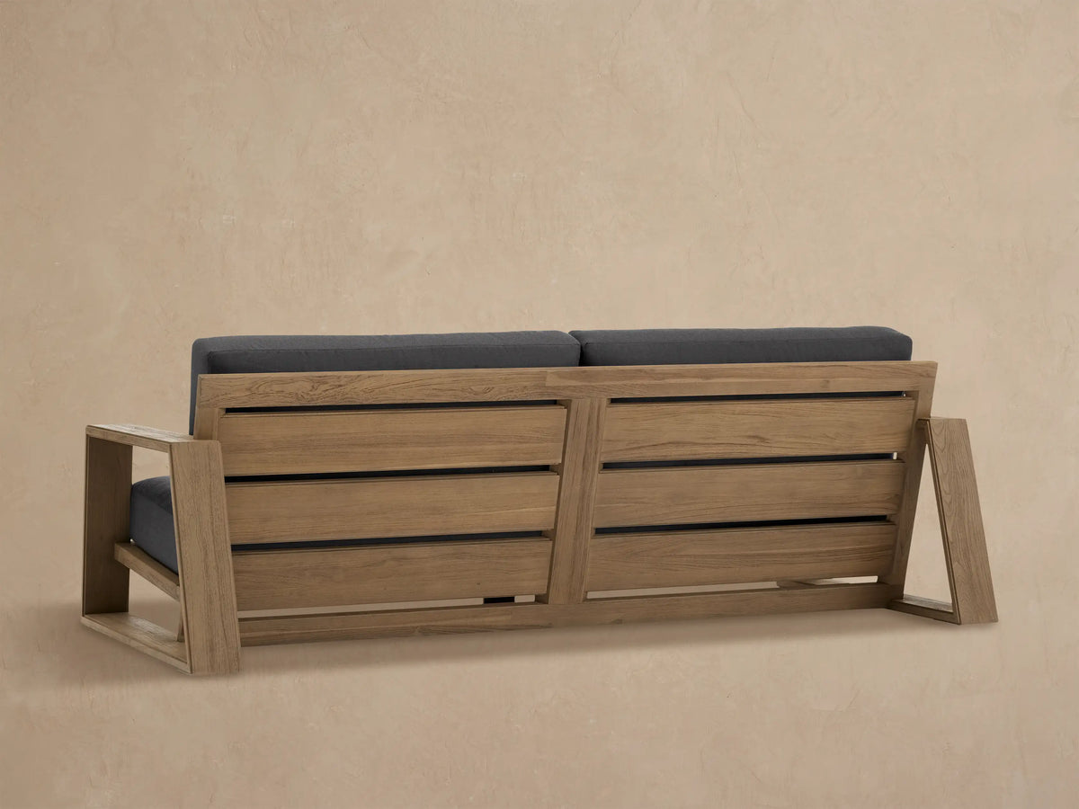 Close-up of a Canyon Outdoor Teak Sofa's light brown distressed armrest and dark gray seat and back cushions.