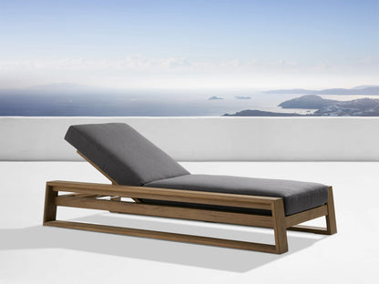 Canyon Outdoor Teak Chaise with an adjustable backrest in a natural teak finish. Gray cushions on a minimalist frame. Scenic ocean view backdrop.