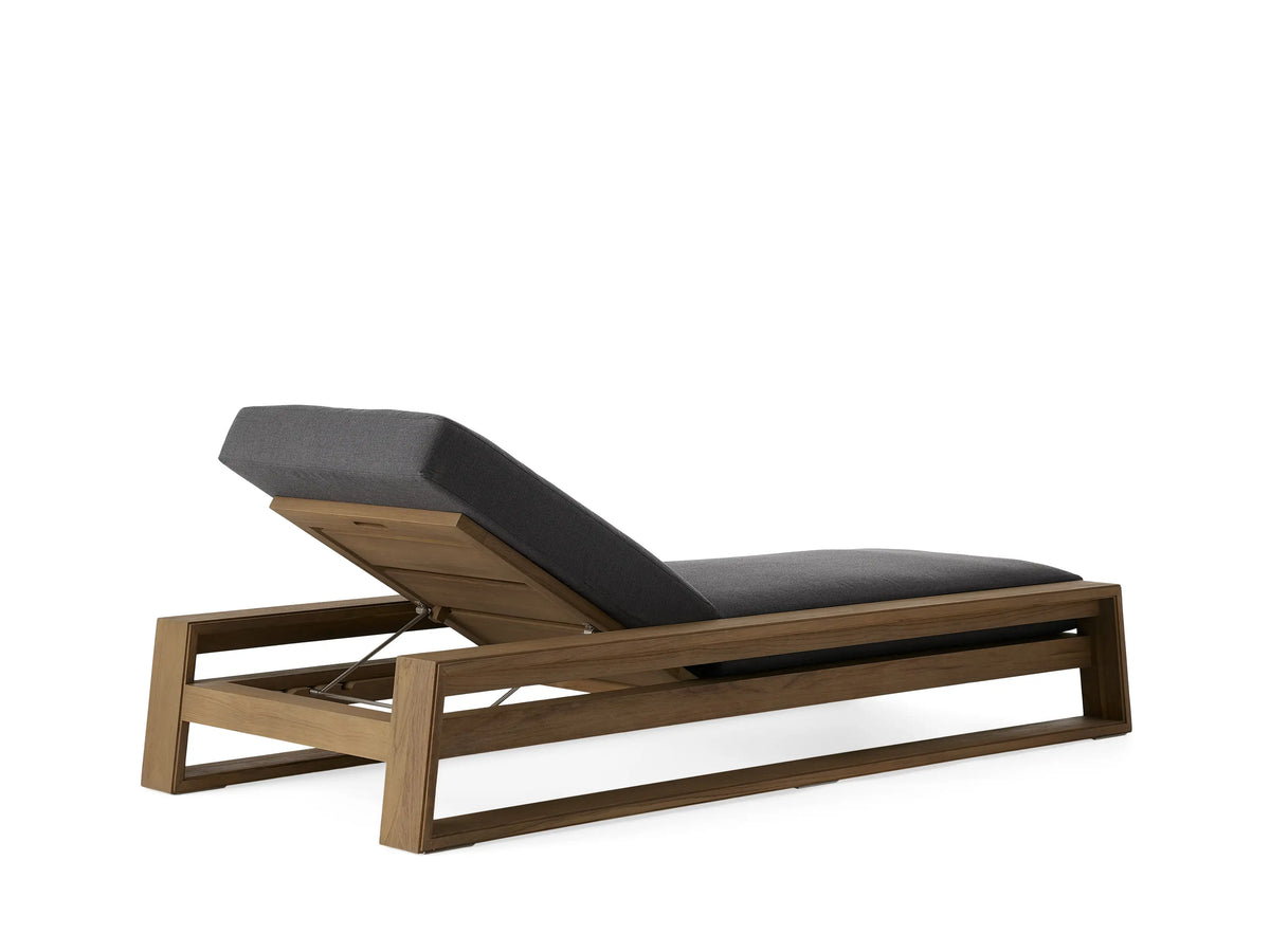 Canyon Outdoor Teak Chaise with an adjustable backrest in a natural teak finish. Gray cushions on a minimalist frame. Scenic ocean view backdrop.