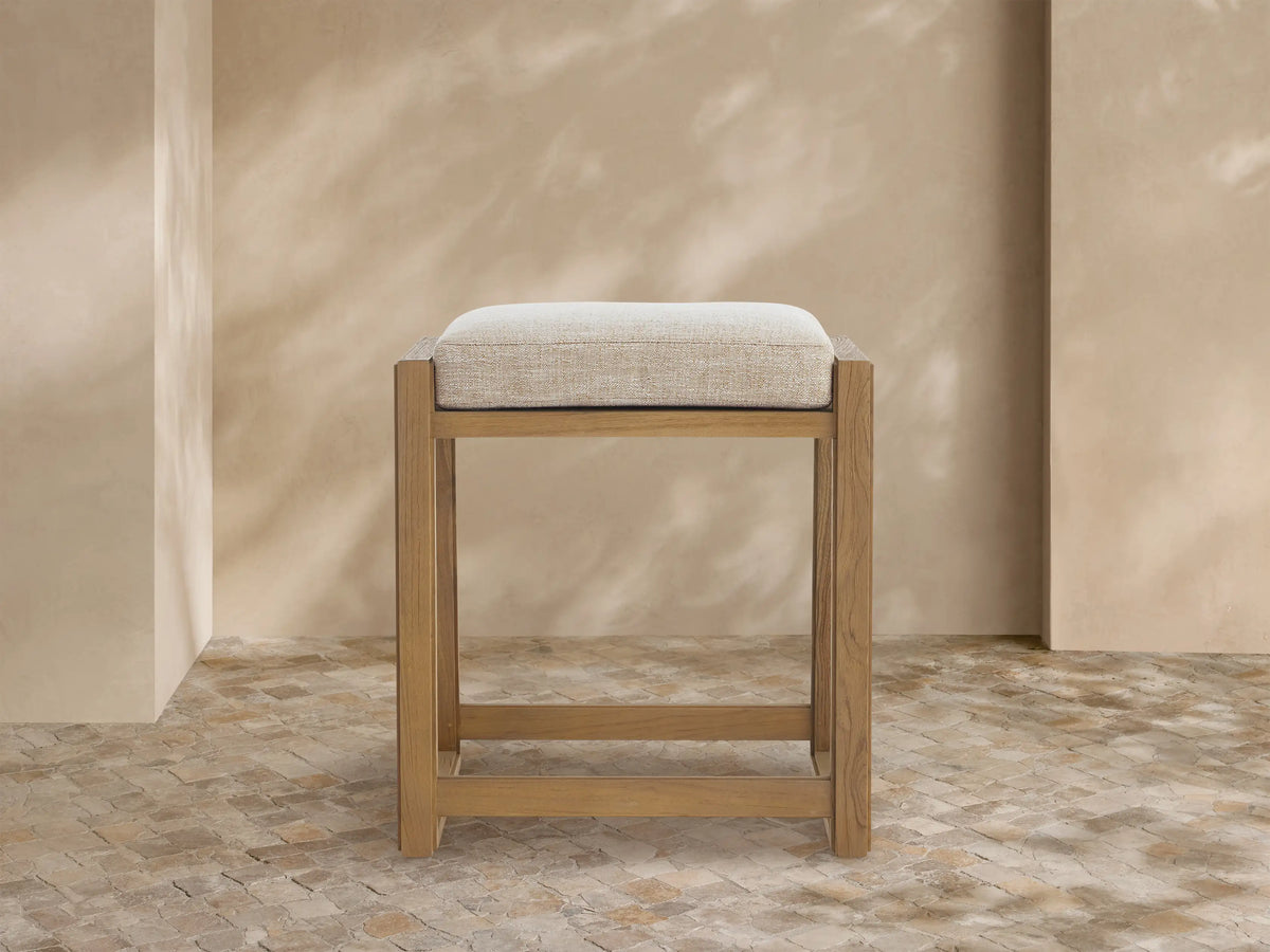 Canyon Outdoor Teak Backless Counter Stool, light teak wood frame, soft Priano Malt cushioned seat, angled left on tiled floor.