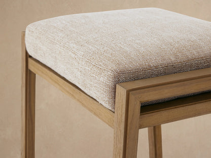 Canyon Outdoor Teak Backless Counter Stool with light brown teak frame & Priano Malt cushion, centered on tan wall/floor.