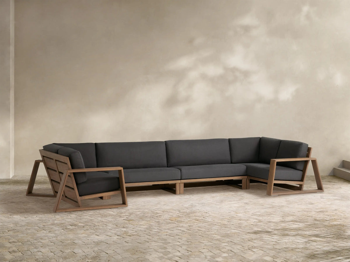 Canyon Outdoor Teak Four-Piece Sectional with dark gray cushions & natural teak frame on a stone patio.