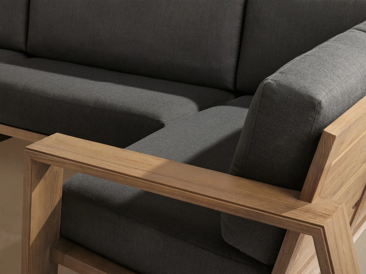 Canyon Outdoor Teak Four-Piece Sectional with dark gray cushions in an L-shape on a paved patio.