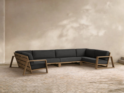 Canyon Outdoor Teak 4-Piece Sectional, U-shaped with dark gray cushions and light brown teak frame on a stone patio.