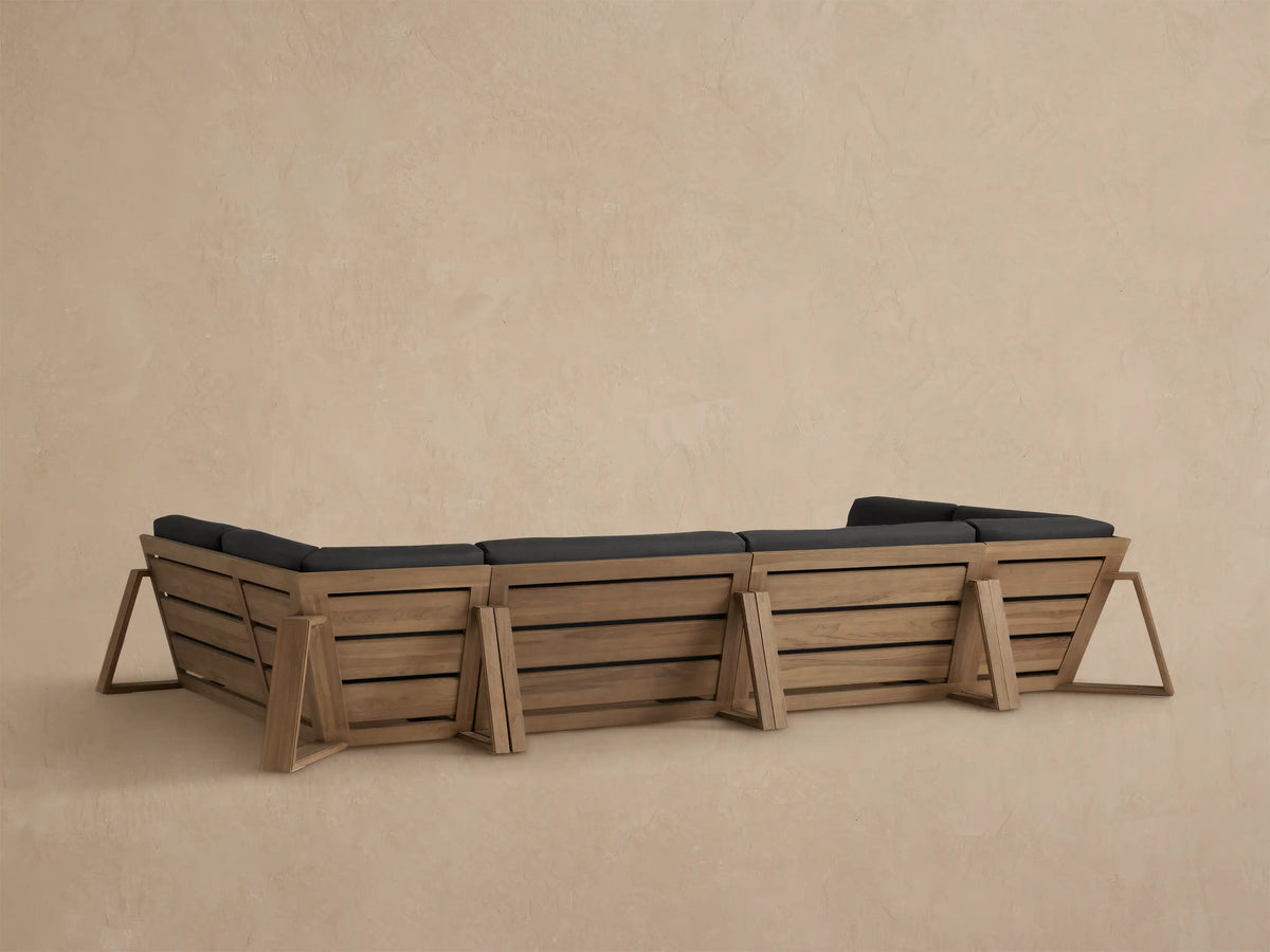 Canyon Outdoor Teak Sectional close-up: light brown teak armrest & dark gray cushions, showing a corner piece.