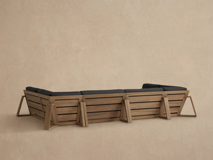 Canyon Outdoor Teak Sectional close-up: light brown teak armrest & dark gray cushions, showing a corner piece.