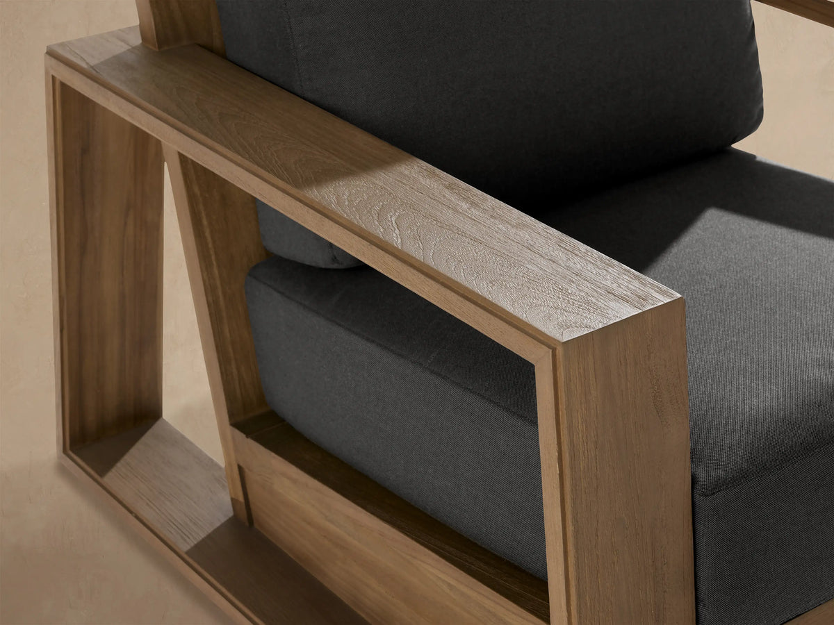 Frontal view of Canyon Outdoor Teak Lounge Chair with a sturdy light teak wood frame and plush dark gray cushions.