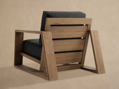 Close-up of Canyon Outdoor Teak Lounge Chair's natural wood armrest and dark grey cushion, angled view.