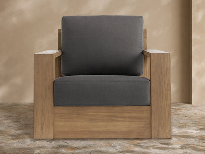 Canyon Outdoor Teak Swivel Chair with light teak wood frame and dark gray cushions, on a stone patio.