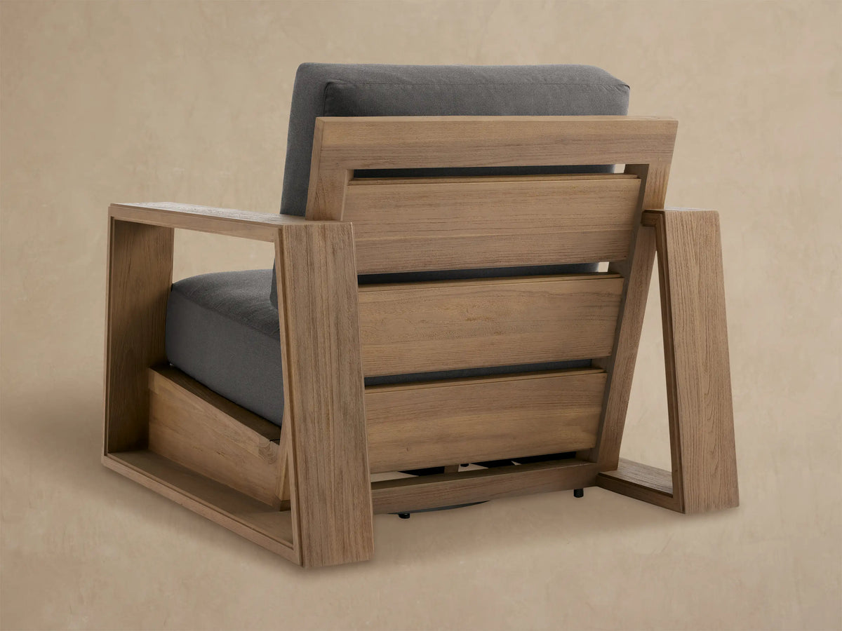 Close-up of a Canyon Outdoor Teak Swivel Chair with a textured light brown teak armrest and dark gray fabric cushions.