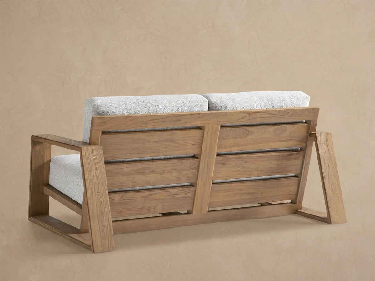 High-angle close-up of Canyon Outdoor Teak Sofa, showing its natural teak frame & light gray textured cushions.