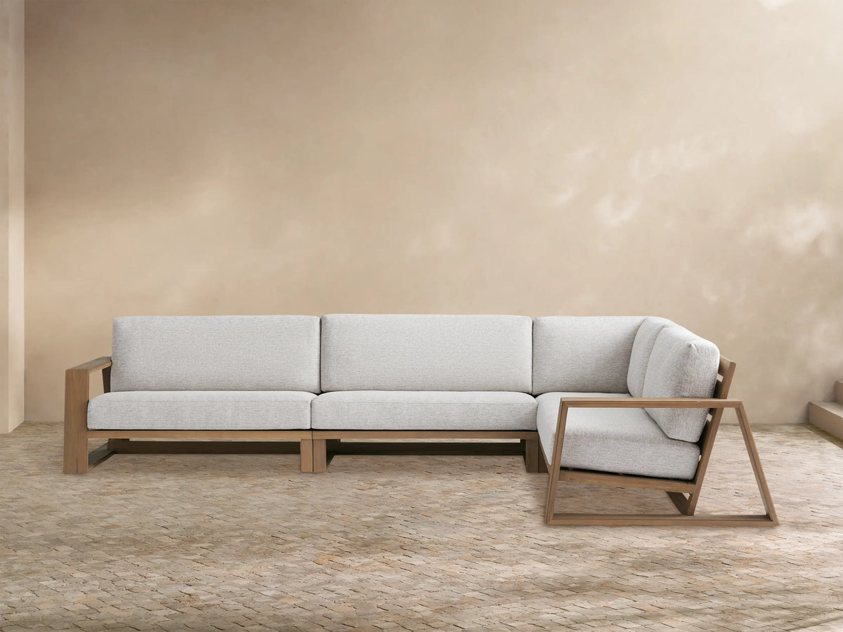 Canyon Outdoor Teak Three-Piece Sectional, L-shaped, with light grey cushions & natural teak wood frame, on a patio.
