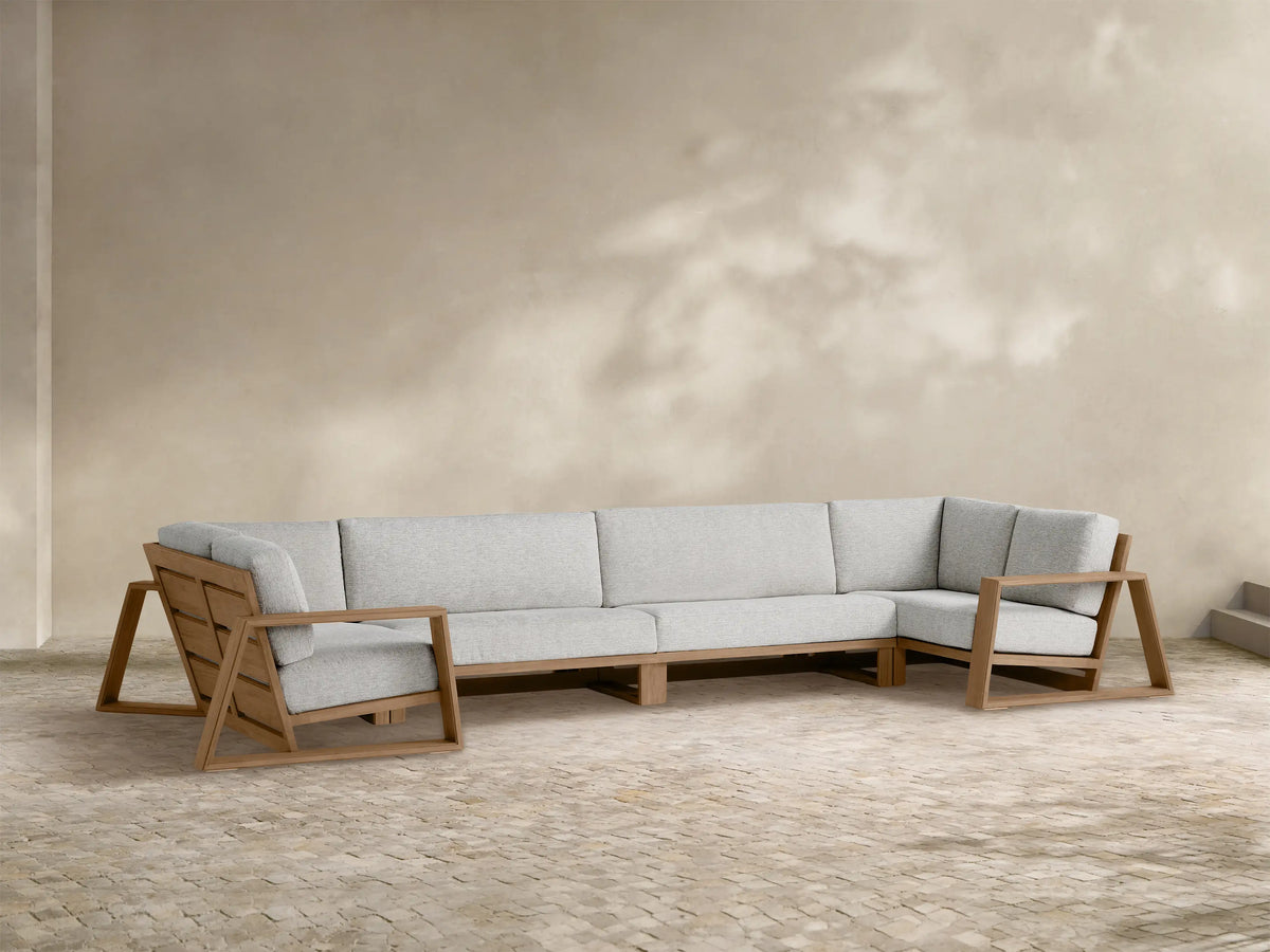 L-shaped Canyon Outdoor Teak Four-Piece Sectional with light grey cushions, open geometric frame, on a stone patio.