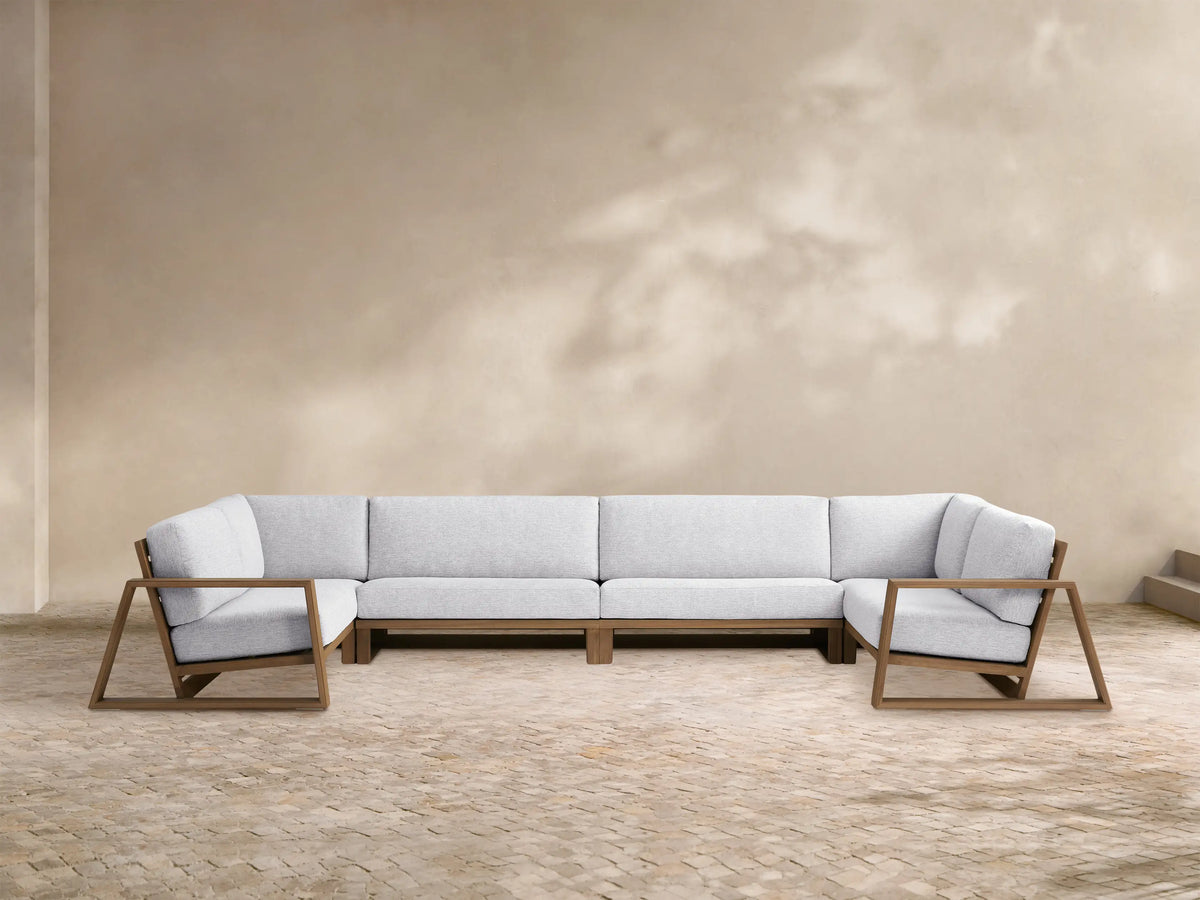 Canyon Outdoor Teak Four-Piece Sectional. L-shaped modular sofa with teak frames & light gray cushions, plus 2 armchairs on a patio.