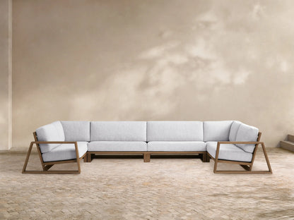 Canyon Outdoor Teak Four-Piece Sectional. L-shaped modular sofa with teak frames & light gray cushions, plus 2 armchairs on a patio.