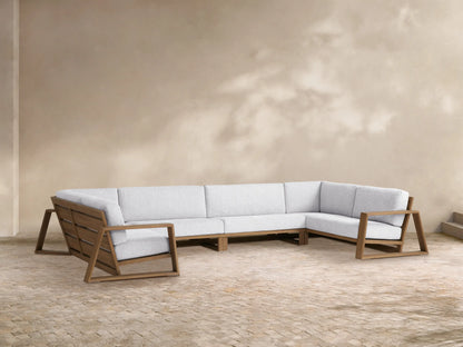 Canyon Outdoor Teak Four-Piece Sectional. L-shaped modular sofa with teak frames & light gray cushions, plus 2 armchairs on a patio.