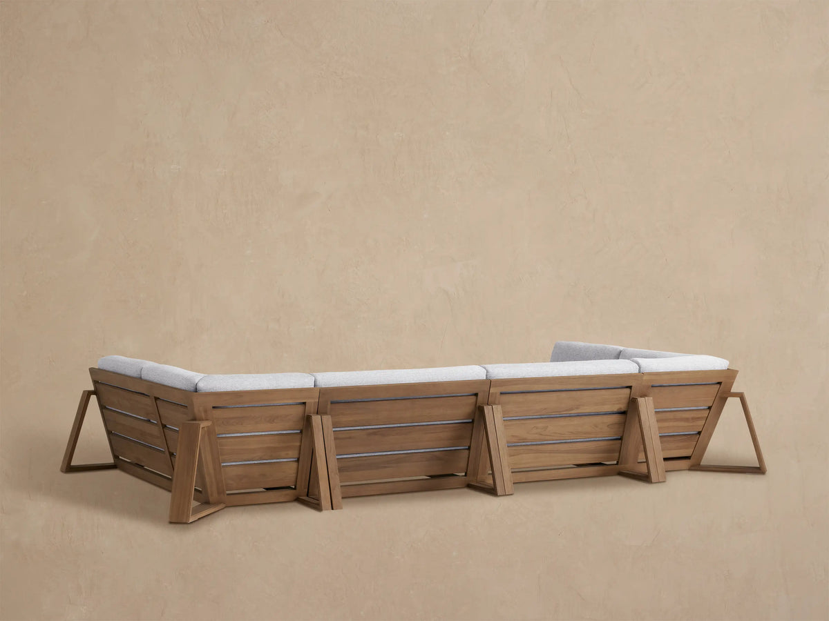 Canyon Outdoor Teak Sectional corner piece, warm brown teak frame, light grey textured cushions, seen from a side angle.