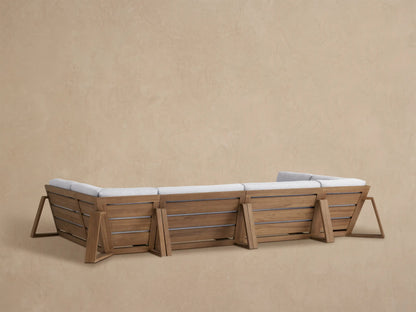 Canyon Outdoor Teak Sectional corner piece, warm brown teak frame, light grey textured cushions, seen from a side angle.