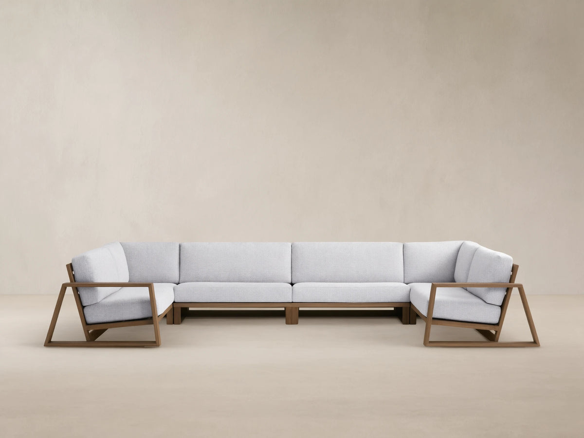 Canyon Outdoor Teak Four-Piece Sectional. L-shaped modular sofa with teak frames & light gray cushions, plus 2 armchairs on a patio.