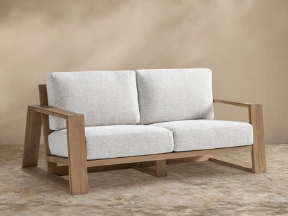 Canyon Outdoor Teak Sofa, a 2-seater with a natural teak wood frame and light grey cushions, on a stone patio.