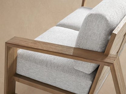 Canyon Outdoor Teak Sofa, 2-seater, with light gray cushions & natural teak wood frame, in an outdoor setting on a paved patio.