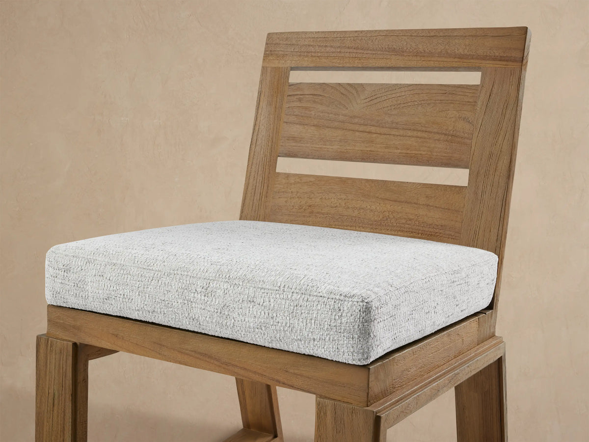 Front view of Canyon Outdoor Teak Dining Side Chair. Natural teak wood frame with two back slats and a light grey fabric seat cushion.
