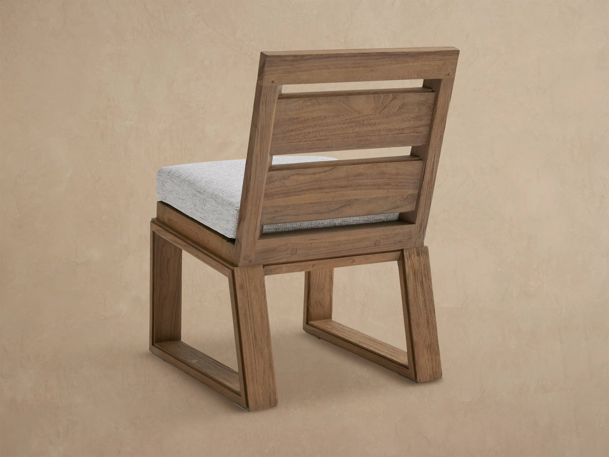 Canyon Outdoor Teak Dining Side Chair with warm brown, textured teak frame, slatted backrest, and light grey fabric cushion.