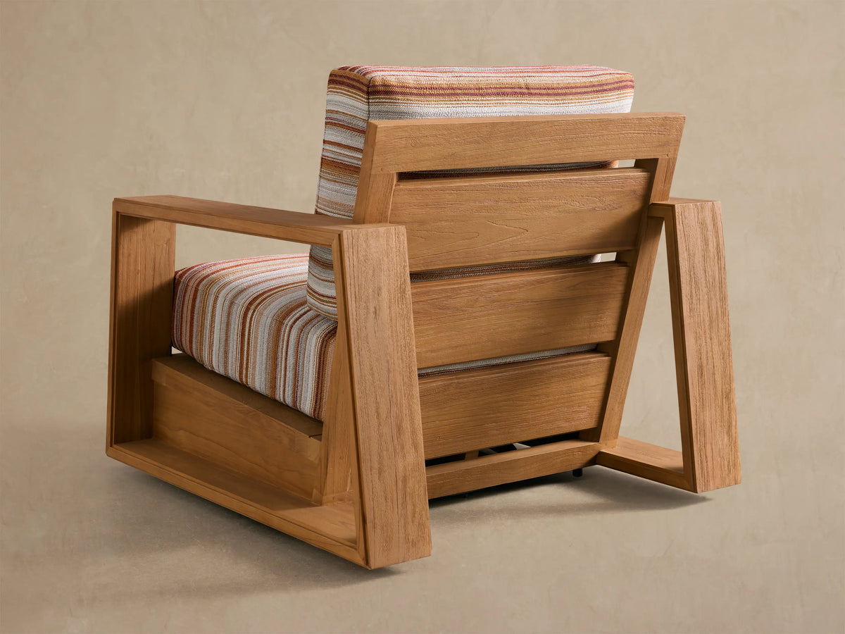 Angled close-up of Canyon Outdoor Teak Swivel Chair. Light brown teak armrest, and back with orange, white, grey striped cushion.