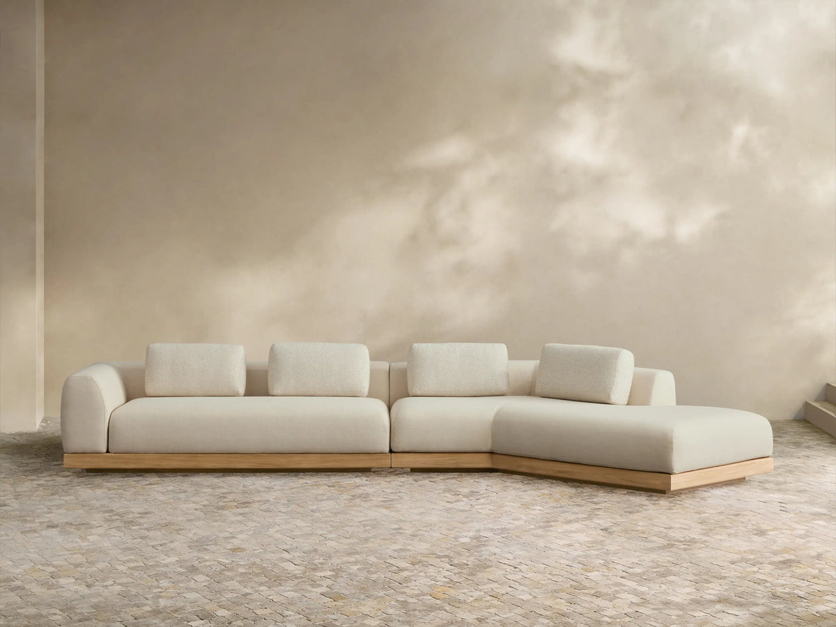 Light cream Carmel Outdoor Two-Piece Bumper Sectional, L-shaped with teak base, lumbar pillows, on a tiled patio.