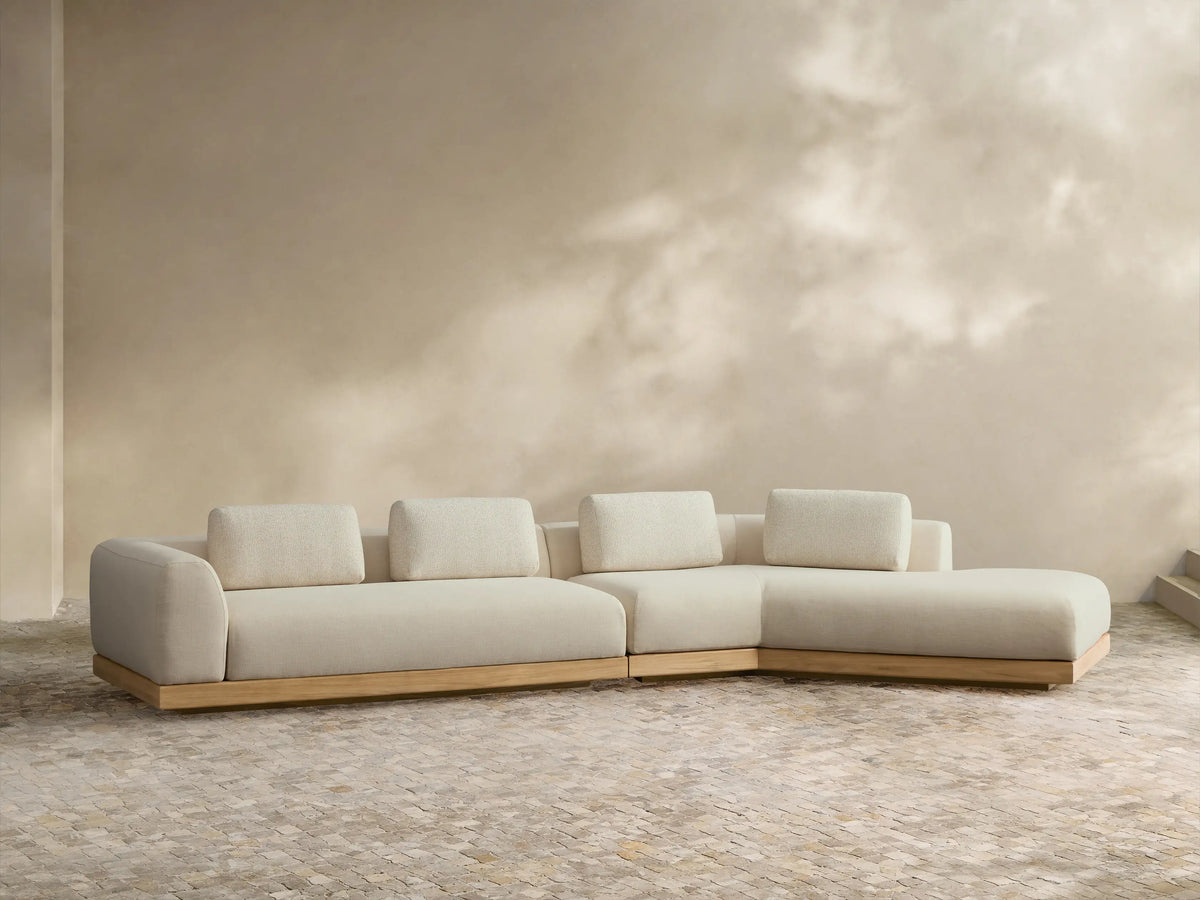 Light cream Carmel Outdoor Two-Piece Bumper Sectional, L-shaped with teak base, lumbar pillows, on a tiled patio.