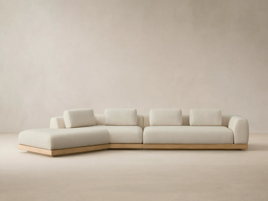 Light cream Carmel Outdoor Two-Piece Bumper Sectional, L-shaped with teak base, lumbar pillows, on a tiled patio.