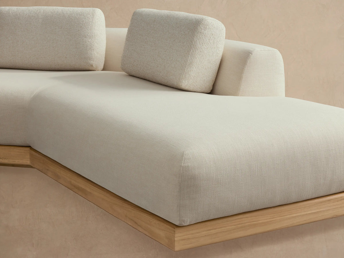 Carmel Outdoor Two-Piece Bumper Sectional, L-shaped, beige cushions, teak base, on patterned floor against warm wall.